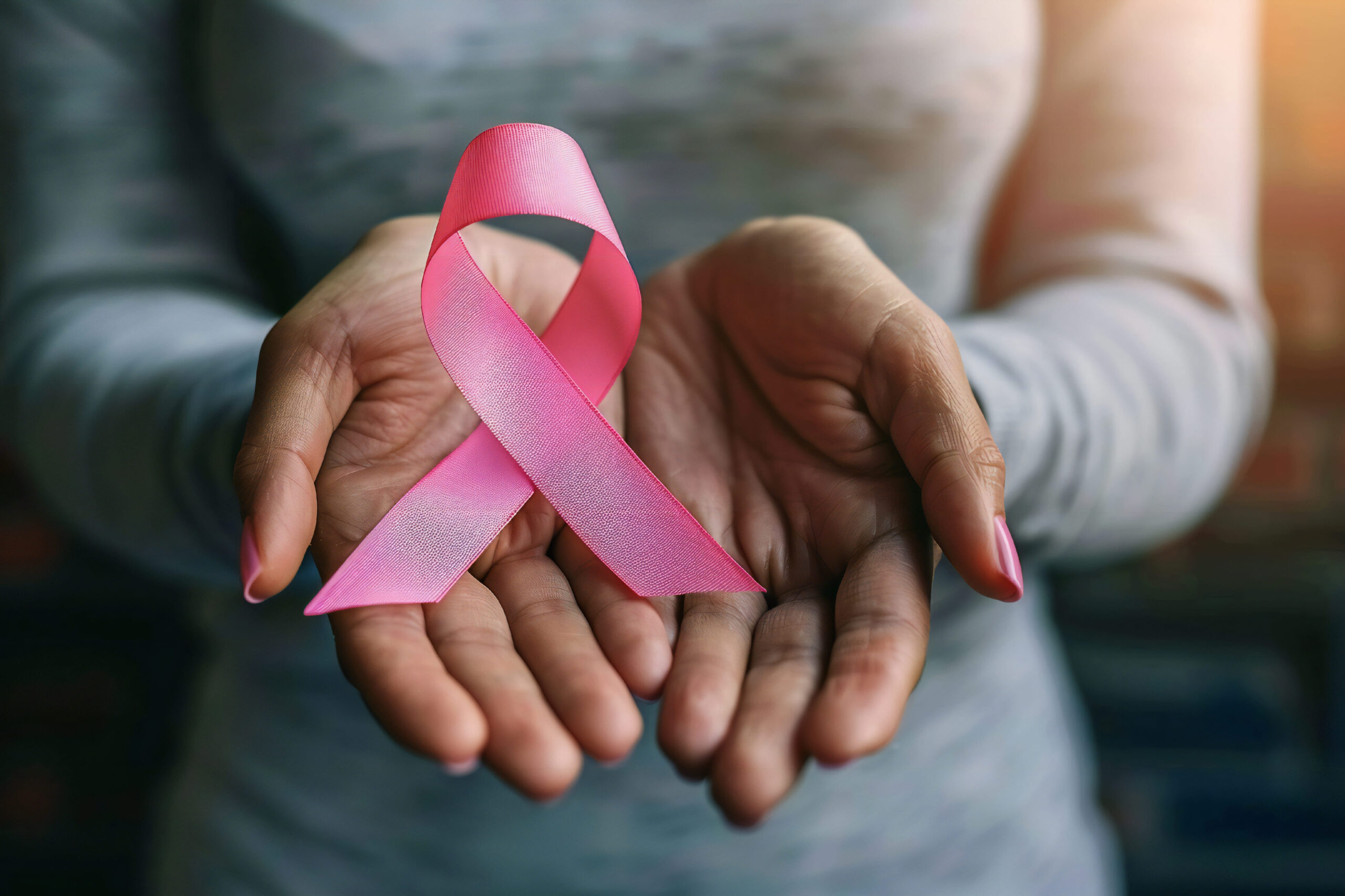 A closeup of a woman cradling a pink breast cancer ribbon as an image of breast cancer survival rates
